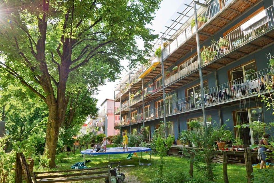Grüner Innenhof mit Bäumen, Trampolin und Laubengängen an einem Wohnhaus