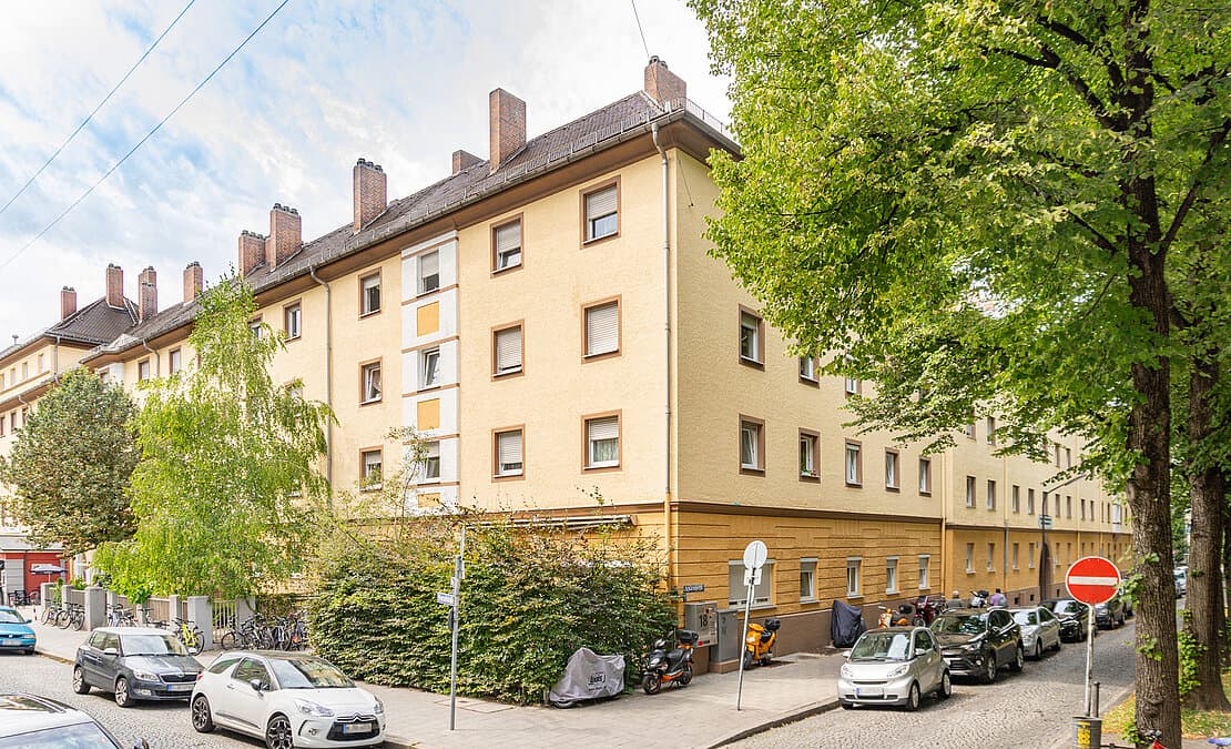 Gelbes Wohnhaus der Genossenschaft ebm München an einer Straßenecke mit Bäumen