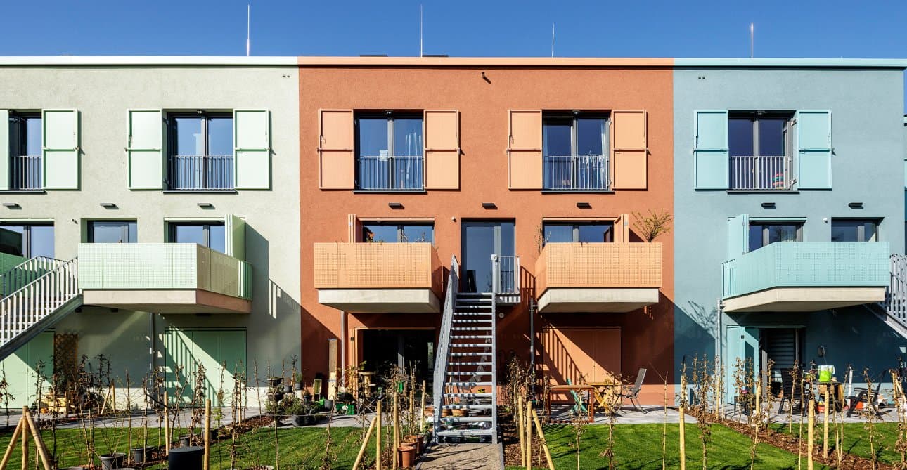 Neue Reihenhäuser der Genossenschaft Die Ehrenfelder mit grüner, terrakottafarbener und blauer Fassade und Gärten