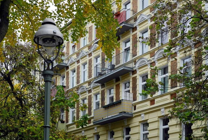 Gründerzeit-Wohnhaus mit Balkonen hinter Herbstbäumen und einer Straßenlaterne