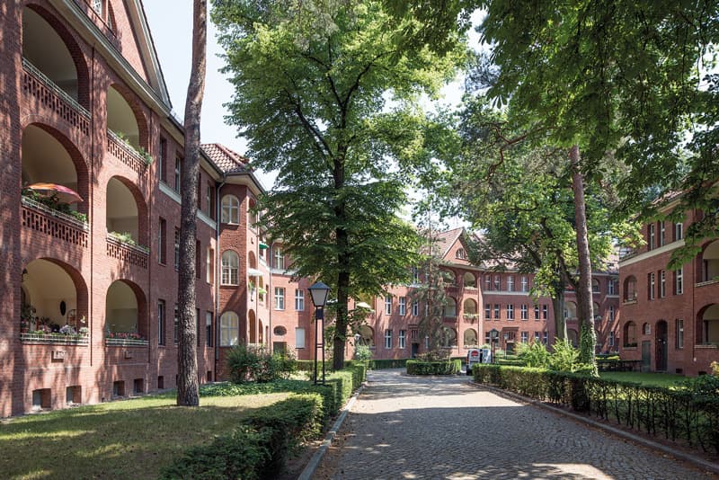 Ruhiger Innenhof einer Backstein-Siedlung mit alten Bäumen